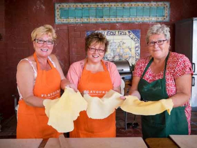 Three guests in apron preparing pizza dough.